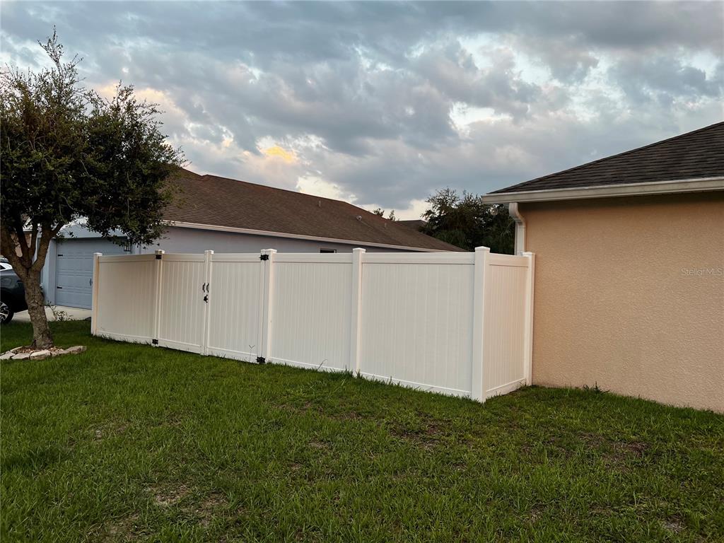 A white vinyl privacy fence stands in a grassy backyard between two residential houses — 3460 BELLERICAY LANE, LAND O LAKES, FL