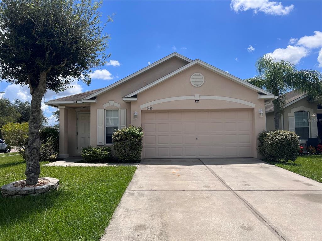 A single-story tan house with a two-car garage, a concrete driveway, and a front lawn — 3460 BELLERICAY LANE, LAND O LAKES, FL