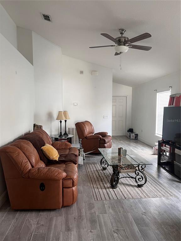 A living room features a brown leather sofa, matching recliner, glass coffee table, and wood-look flooring — 3460 BELLERICAY LANE, LAND O LAKES, FL
