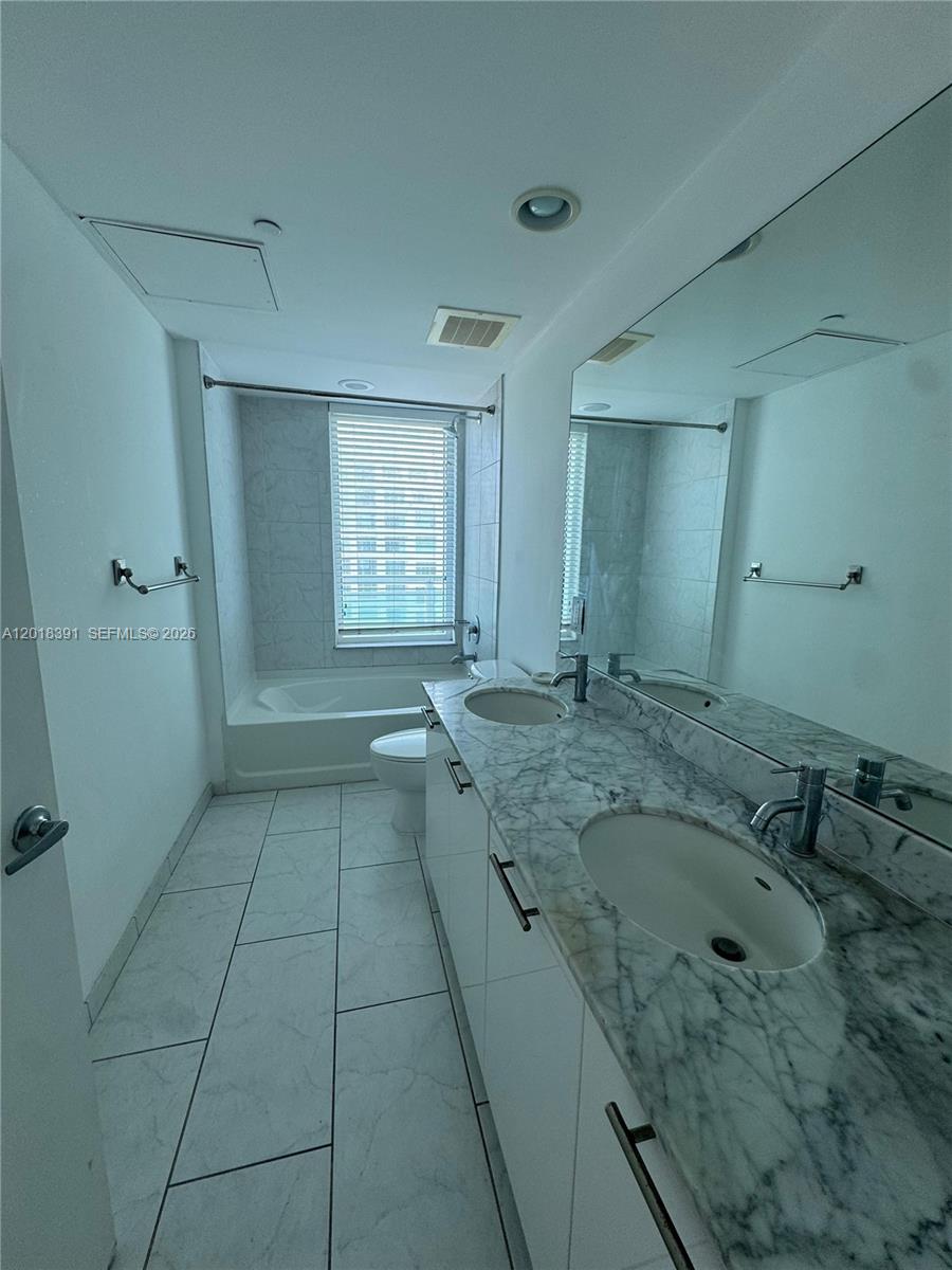 A bathroom features a double vanity with marble countertops, white cabinetry, and a tub-shower combo — 951 N Brickell Ave # 3001, Miami FL 33131, MIAMI, FL