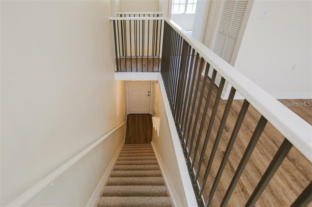 A carpeted staircase leads down to a landing with a white door and wood flooring — 5655 BENTGRASS DRIVE UNIT 9-117, SARASOTA, FL