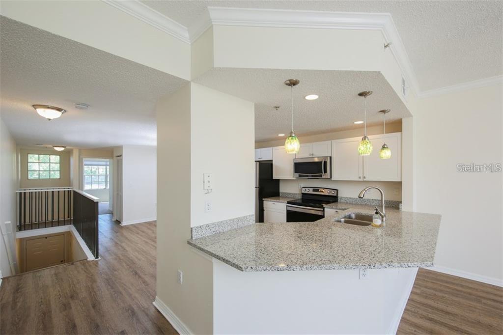 A kitchen with granite countertops and pendant lights overlooks a living area with wood flooring — 5655 BENTGRASS DRIVE UNIT 9-117, SARASOTA, FL