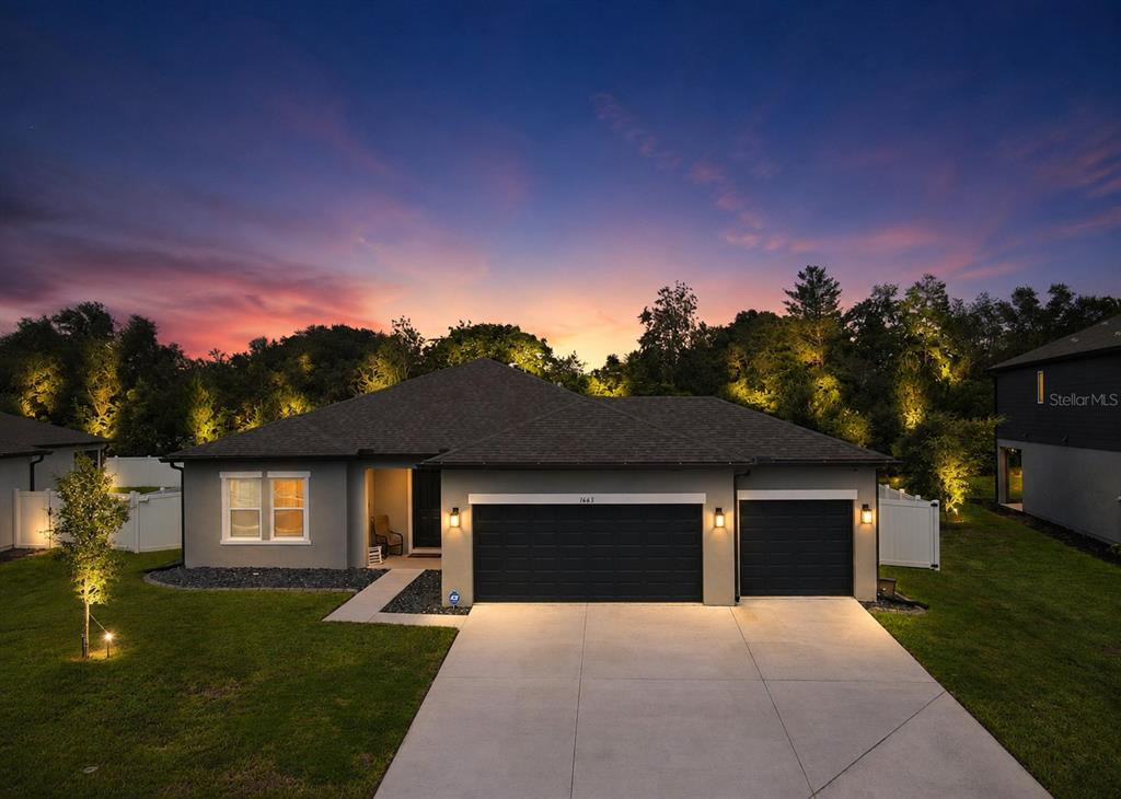 A gray single-story house with a three-car garage at dusk under a colorful sky — 1663 MEADOWLARK DRIVE, DELTONA, FL
