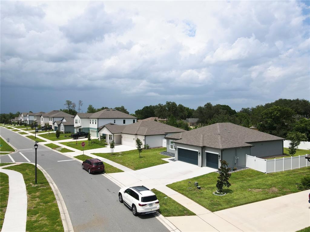 An aerial view shows a suburban street with modern single-family homes and parked cars — 1663 MEADOWLARK DRIVE, DELTONA, FL