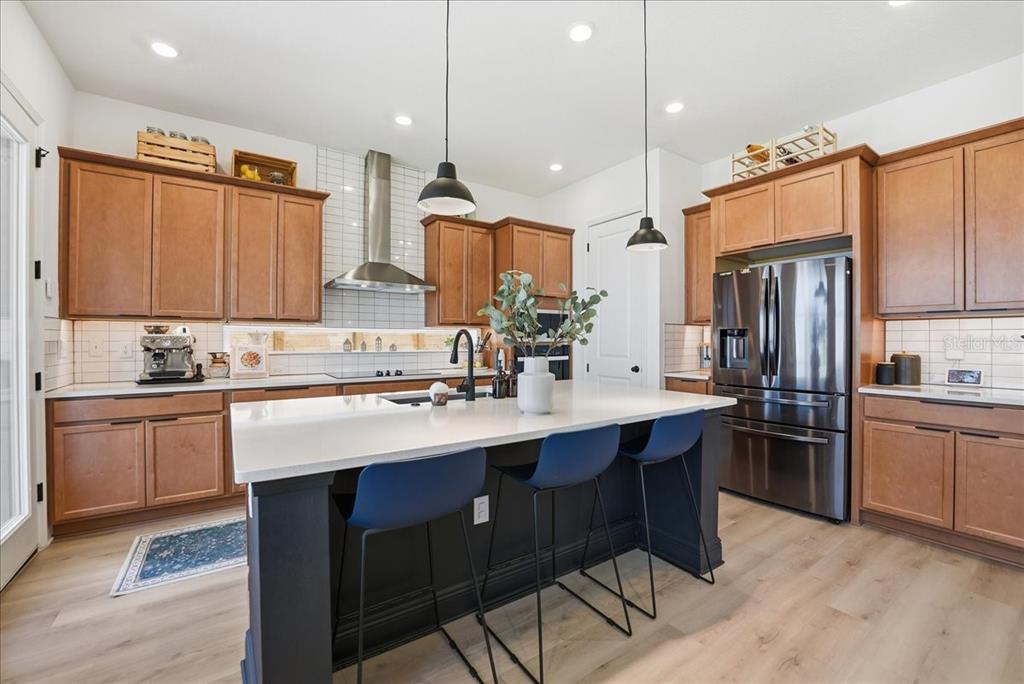 A kitchen features wood cabinets, a dark island with blue stools, and white quartz countertops — 9741 NERUDA STREET, ORLANDO, FL