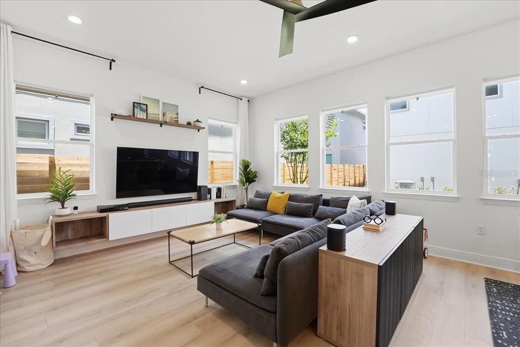 A modern living room features a large sectional sofa, a wall-mounted television, and light wood flooring — 9741 NERUDA STREET, ORLANDO, FL