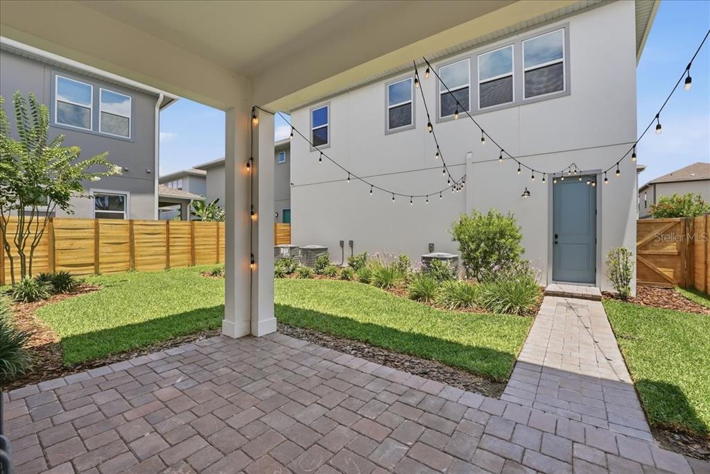 A paved patio overlooks a small backyard with a lawn, landscaping, and string lights — 9741 NERUDA STREET, ORLANDO, FL