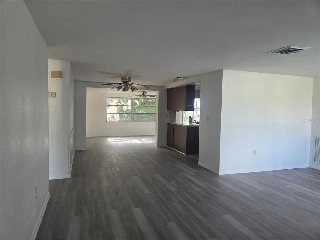 An open-concept living area features gray wood-look flooring, white walls, and a kitchen with dark cabinets — 12213 PARTRIDGE HILL ROW, HUDSON, FL