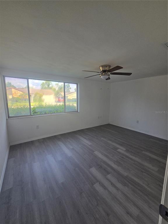 An empty room features white walls, gray wood-look flooring, a ceiling fan, and a large window — 12213 PARTRIDGE HILL ROW, HUDSON, FL