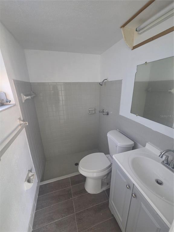 A small bathroom features a walk-in shower, a white toilet, and a gray vanity — 12213 PARTRIDGE HILL ROW, HUDSON, FL