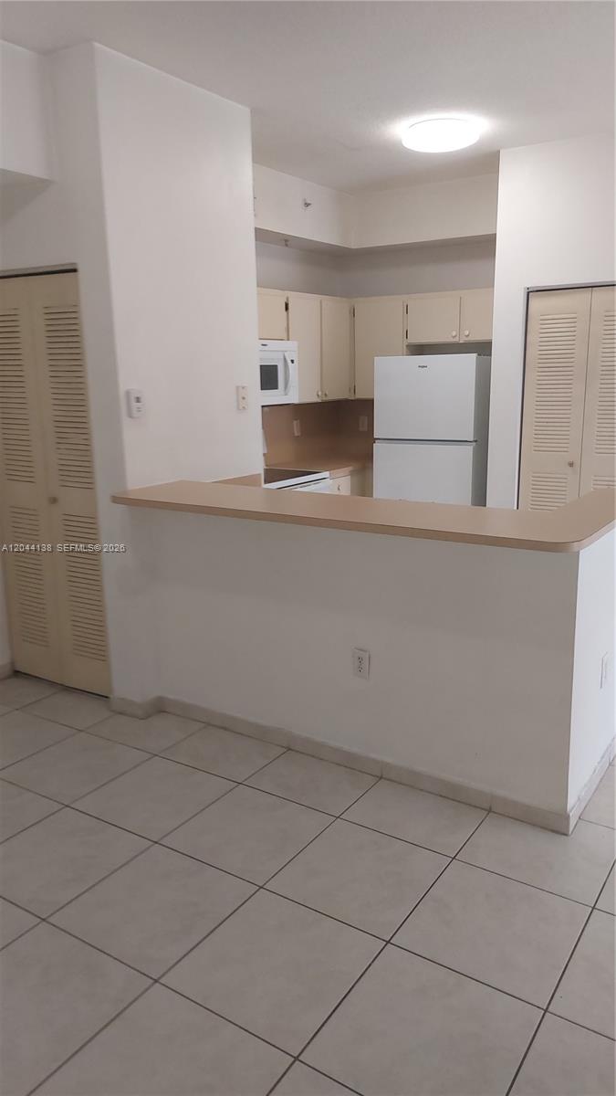 A kitchen with white cabinets and appliances features a breakfast bar overlooking a tiled room — 7290 NW 114th Ave # 7, Doral FL 33178, DORAL, FL
