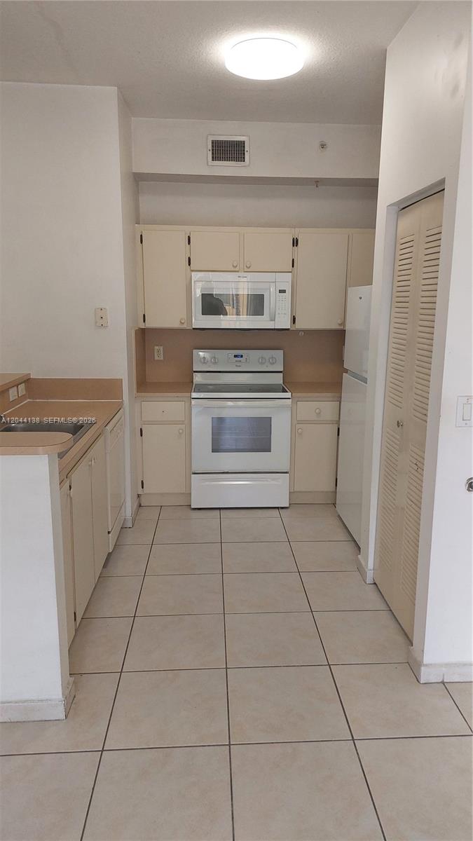 A kitchen features white appliances, beige cabinets, laminate countertops, and light-colored floor tiles — 7290 NW 114th Ave # 7, Doral FL 33178, DORAL, FL