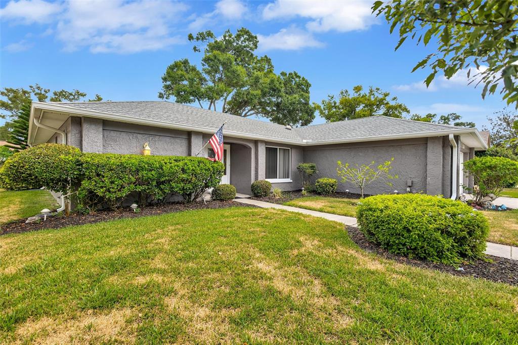 A gray, single-story house with a lawn, landscaping, and an American flag by the entrance — 1743 MACDONNELL DRIVE, PALM HARBOR, FL