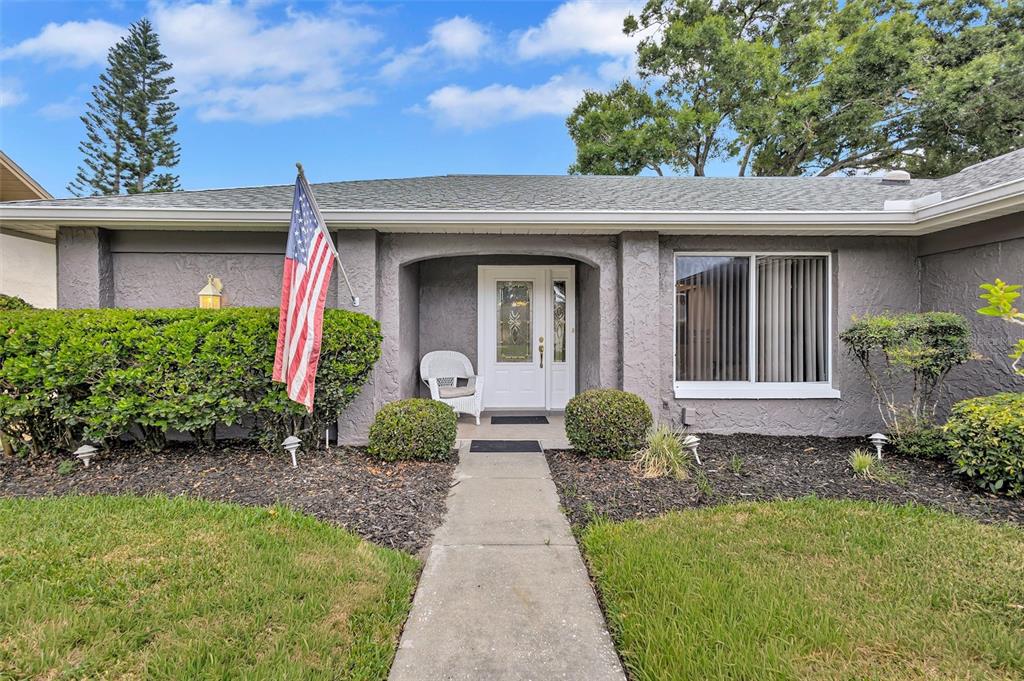 A gray single-story house features a white front door, a walkway, and a front lawn — 1743 MACDONNELL DRIVE, PALM HARBOR, FL