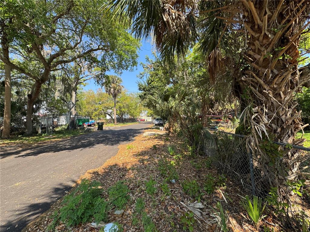 A paved street lined with trees and palm trees runs past a chain-link fence — 1127 MARTHA DRIVE, DAYTONA BEACH, FL