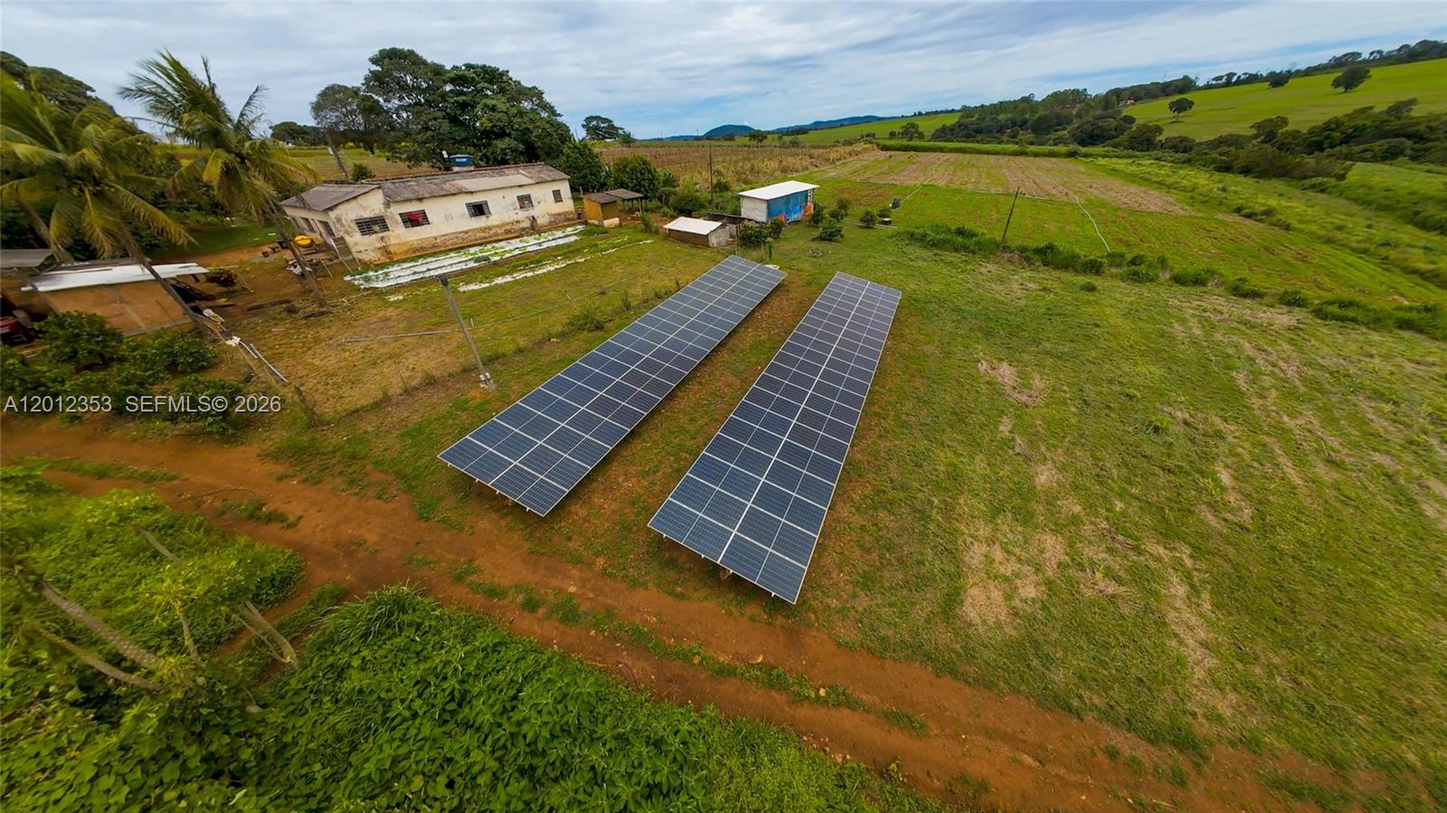 An aerial view shows two ground-mounted solar panel arrays on a rural property with buildings — BR153 km114, GO, GO