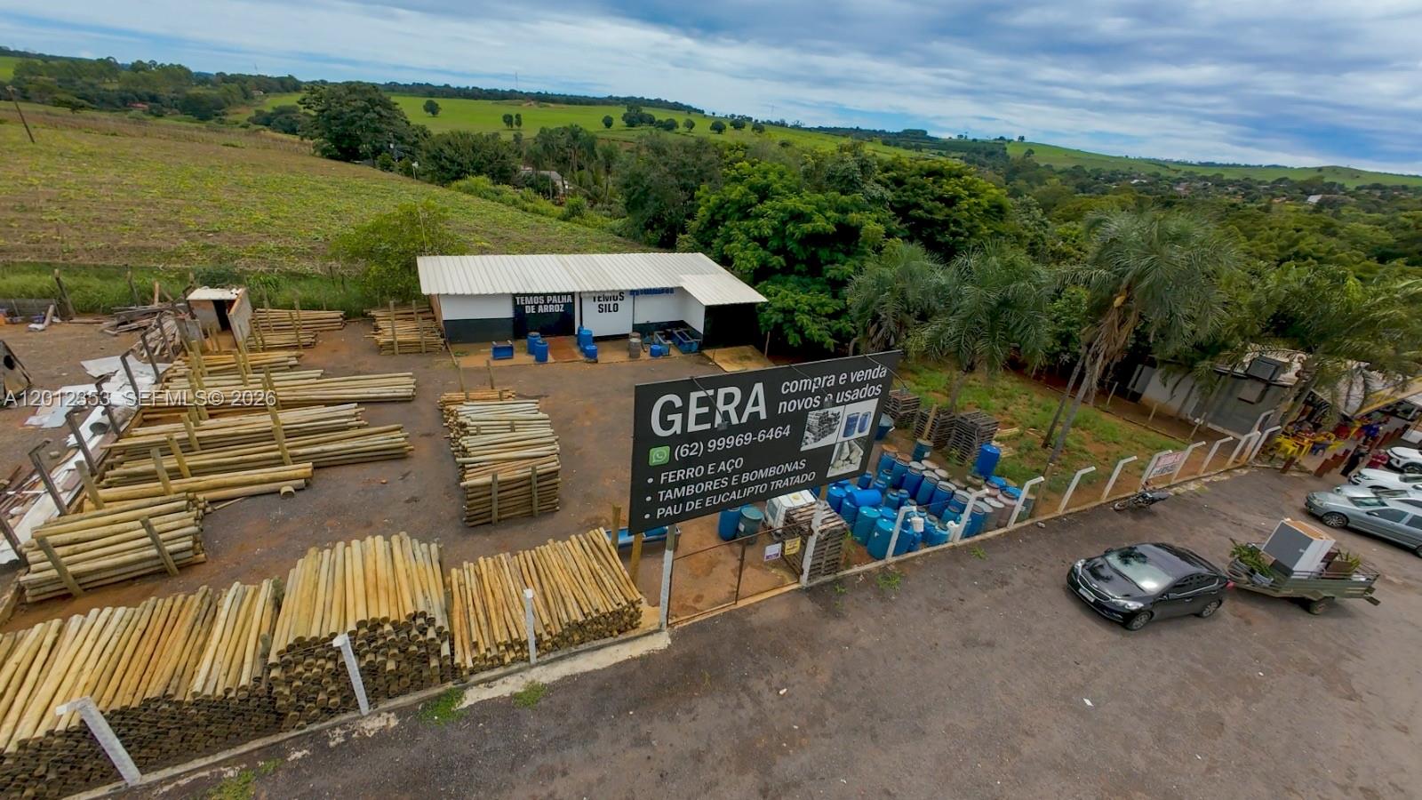 An aerial view shows a business yard with stacked wooden poles and blue drums — BR153 km114, GO, GO