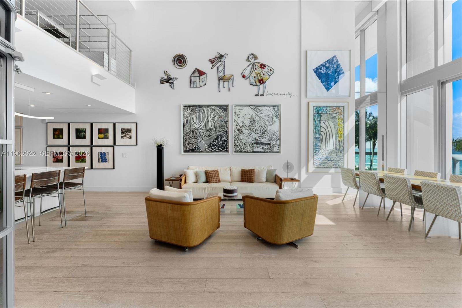 A spacious living room features high ceilings, large windows, modern furniture, and extensive wall art — 6899 Collins Ave # 403, Miami Beach FL 33141, MIAMI BEACH, FL