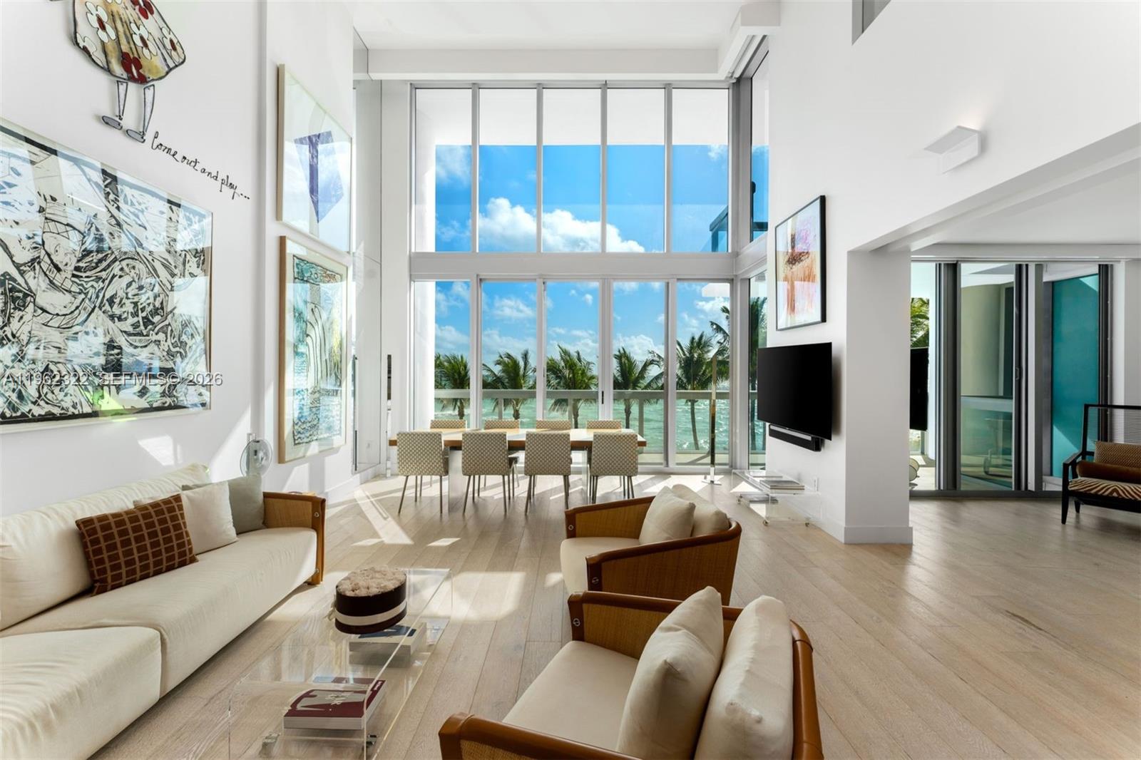 A bright, double-height living and dining area features floor-to-ceiling windows overlooking the ocean — 6899 Collins Ave # 403, Miami Beach FL 33141, MIAMI BEACH, FL