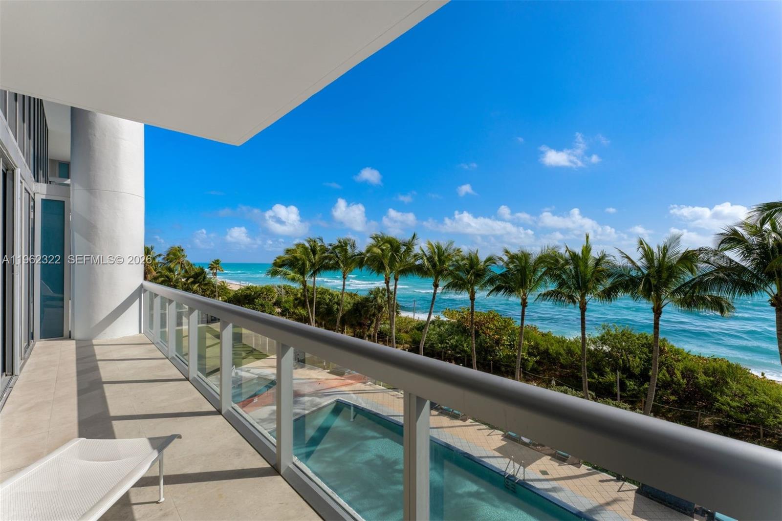 A balcony overlooks a swimming pool, palm trees, and the ocean under a clear sky — 6899 Collins Ave # 403, Miami Beach FL 33141, MIAMI BEACH, FL
