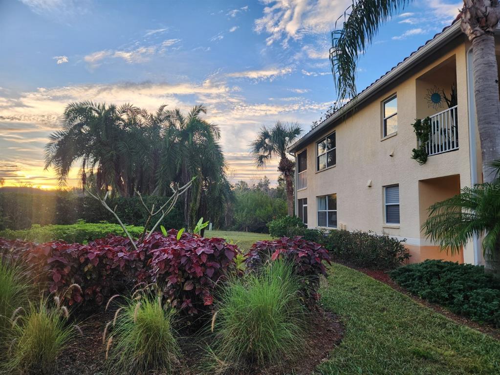A multi-story apartment building exterior with landscaping and palm trees under a sunset sky — 4442 CORSO VENETIA BOULEVARD UNIT A14, VENICE, FL