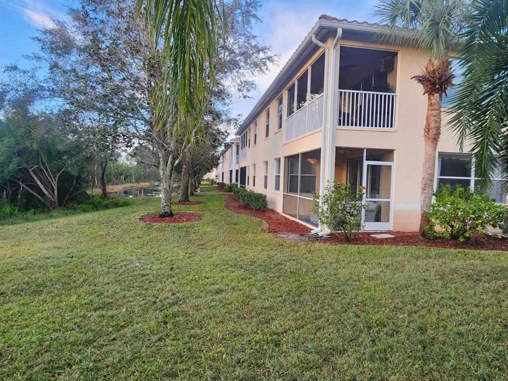 Exterior view of a multi-story apartment building with screened balconies and a grassy yard — 4442 CORSO VENETIA BOULEVARD UNIT A14, VENICE, FL