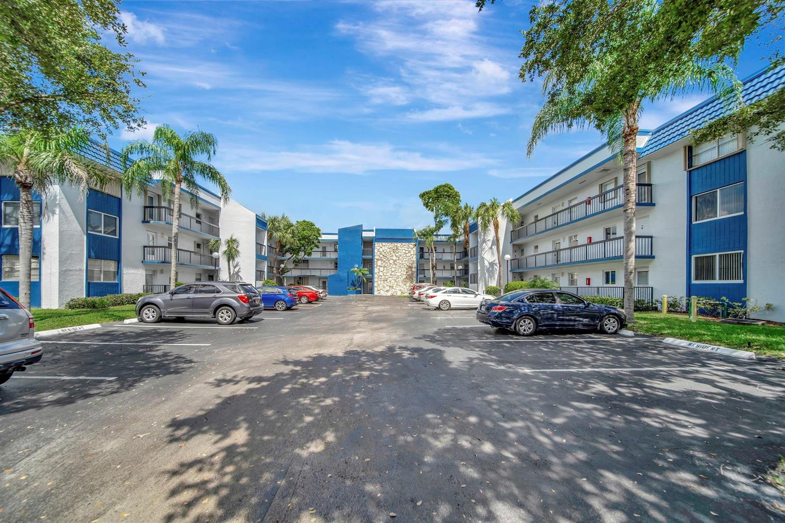 A parking lot sits between two multi-story apartment buildings with blue accents and palm trees — 3100 Holiday Springs Boulevard # 305, Margate FL 33063, MARGATE, FL