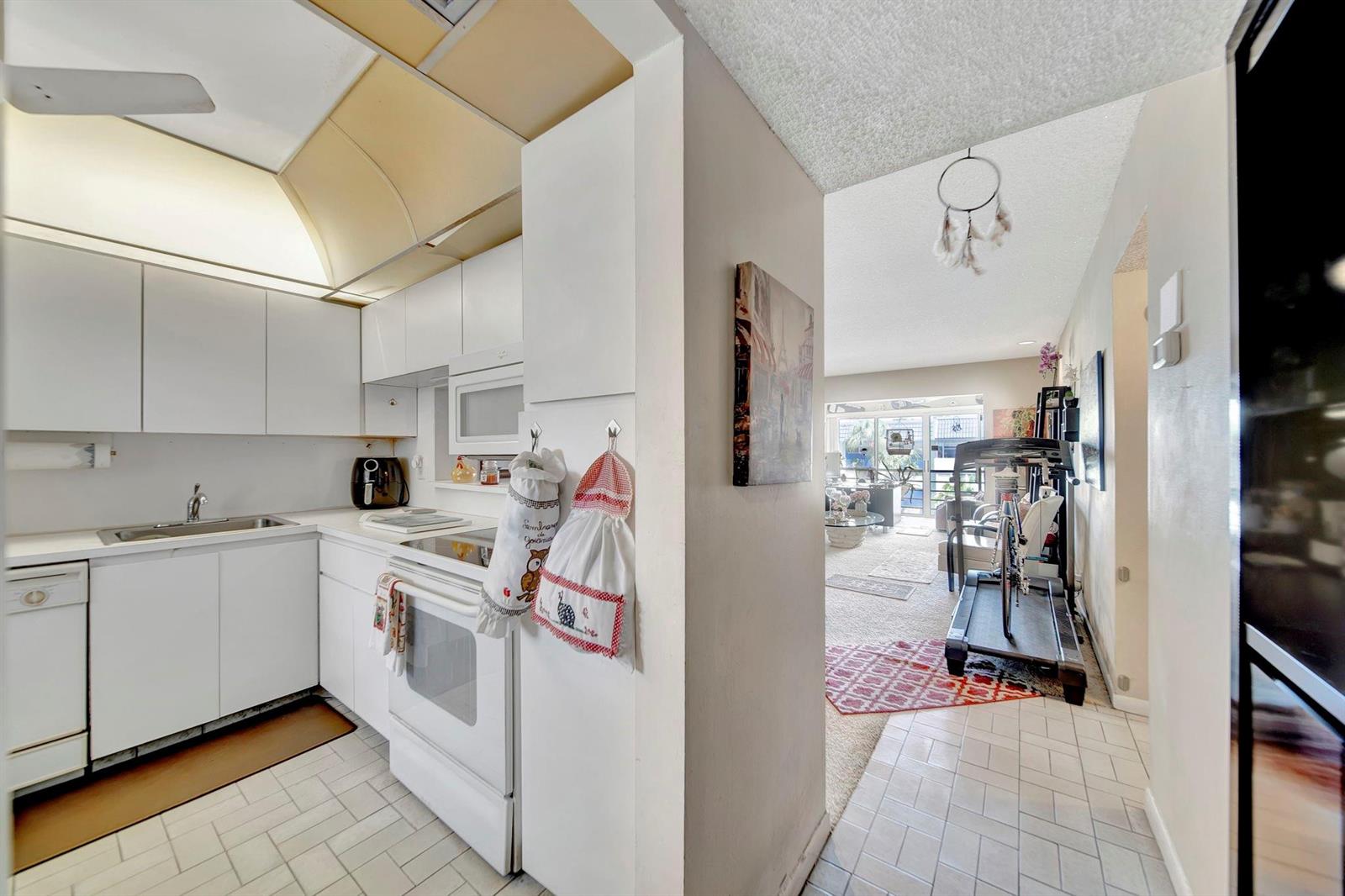 A white kitchen with a stove and sink opens into a living area with carpet — 3100 Holiday Springs Boulevard # 305, Margate FL 33063, MARGATE, FL