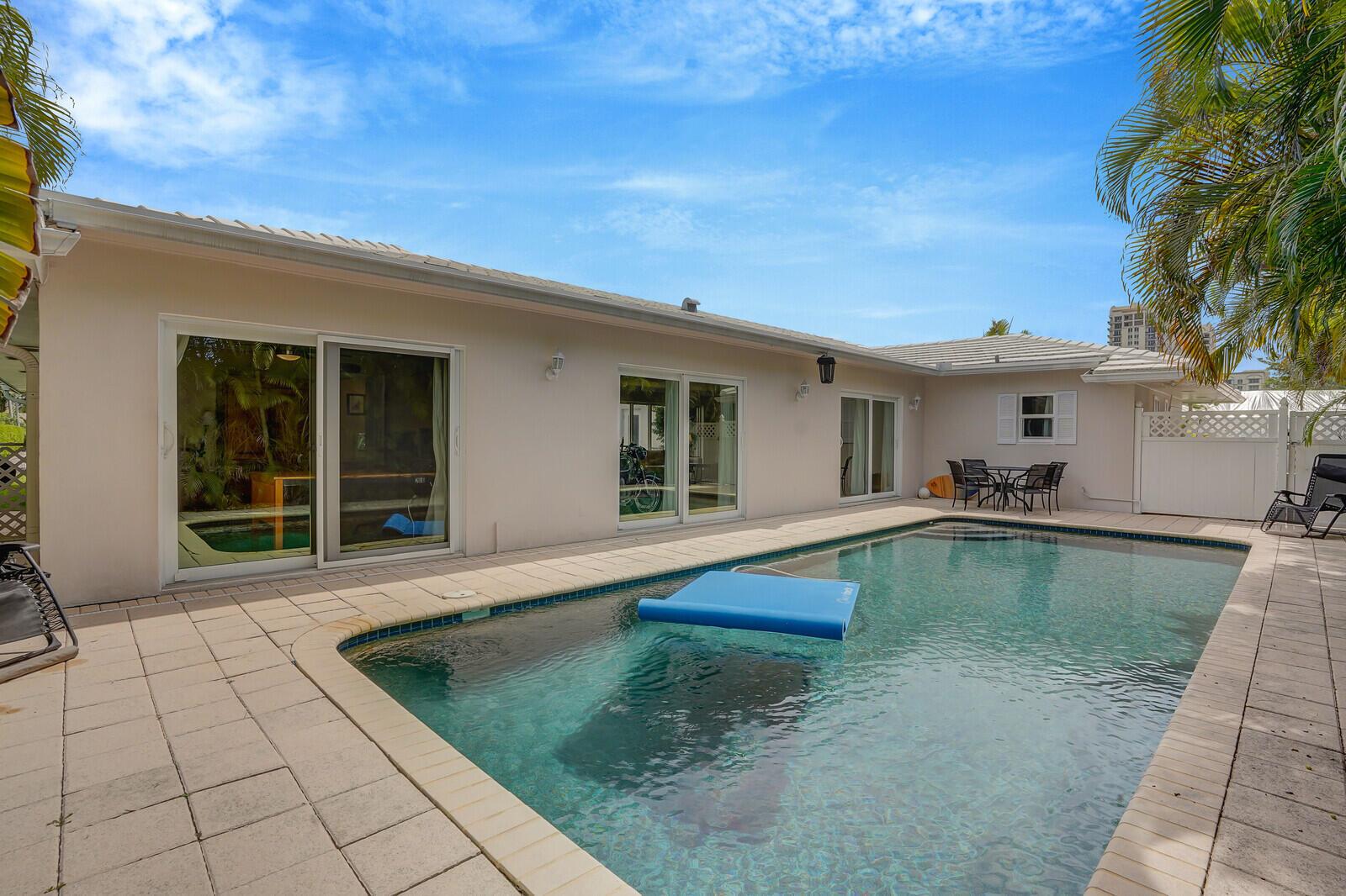 A backyard swimming pool sits adjacent to a beige house with sliding glass doors — 1211 Bimini Lane, Singer Island FL 33404, SINGER ISLAND, FL