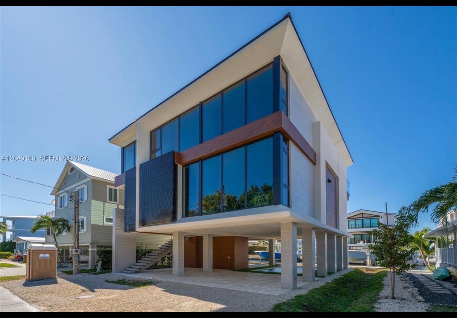 A modern, elevated two-story house with large glass windows stands on concrete pilings — KEY LARGO, FL