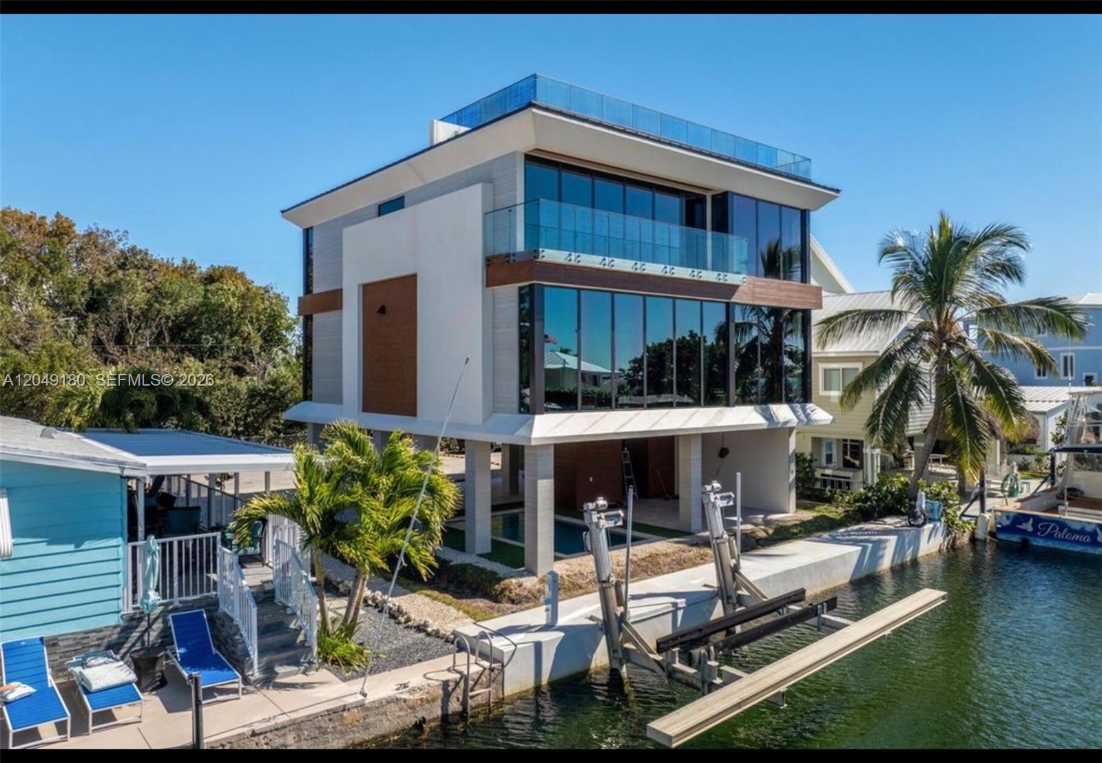 A modern three-story waterfront home with a pool, glass balconies, and a private boat lift — KEY LARGO, FL