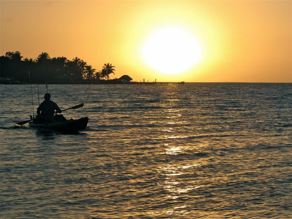 A person paddles a kayak on the water during a bright sunset near a shoreline — 15447 ARON CIRCLE, PORT CHARLOTTE, FL