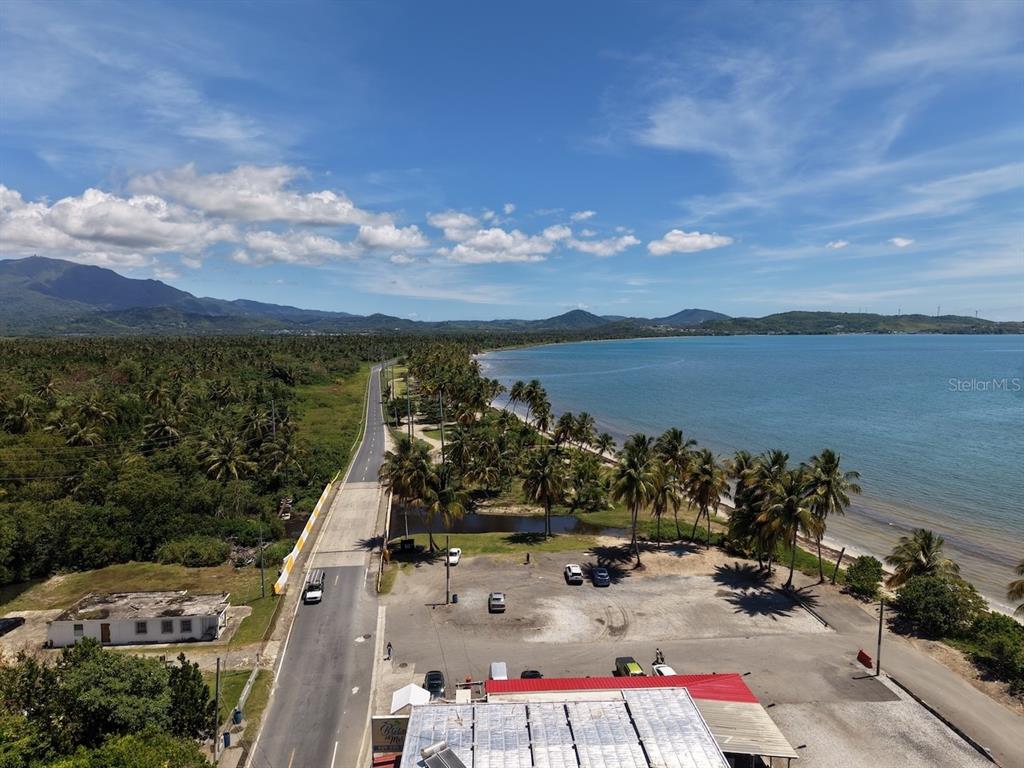 An aerial view shows a coastal road, palm trees, a beach, and nearby mountains — 10 (70) DOCTOR. VIDAL ST. (PR-3), PUNTA SANTIAGO, PR
