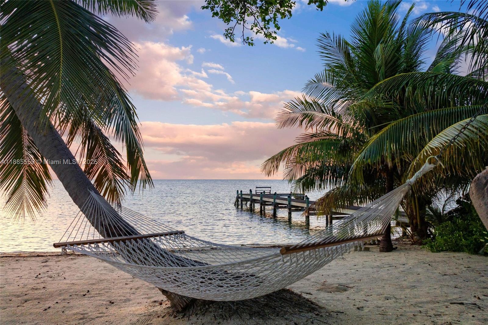 A white rope hammock hangs between two palm trees on a sandy beach overlooking water — 109 Columbus Dr, Islamorada FL 33036, ISLAMORADA, FL