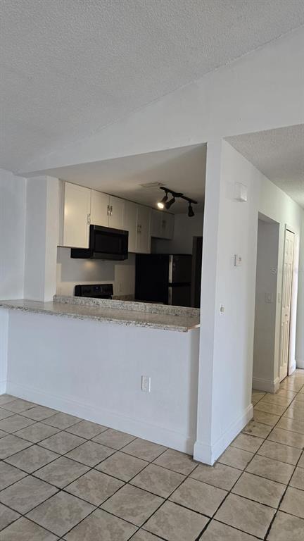 A kitchen with white cabinets and a granite breakfast bar overlooks a tiled living area — 5214 VIA HACIENDA CIRCLE UNIT A307, ORLANDO, FL