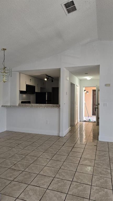 A kitchen with a breakfast bar overlooks a tiled living area leading to an entryway — 5214 VIA HACIENDA CIRCLE UNIT A307, ORLANDO, FL