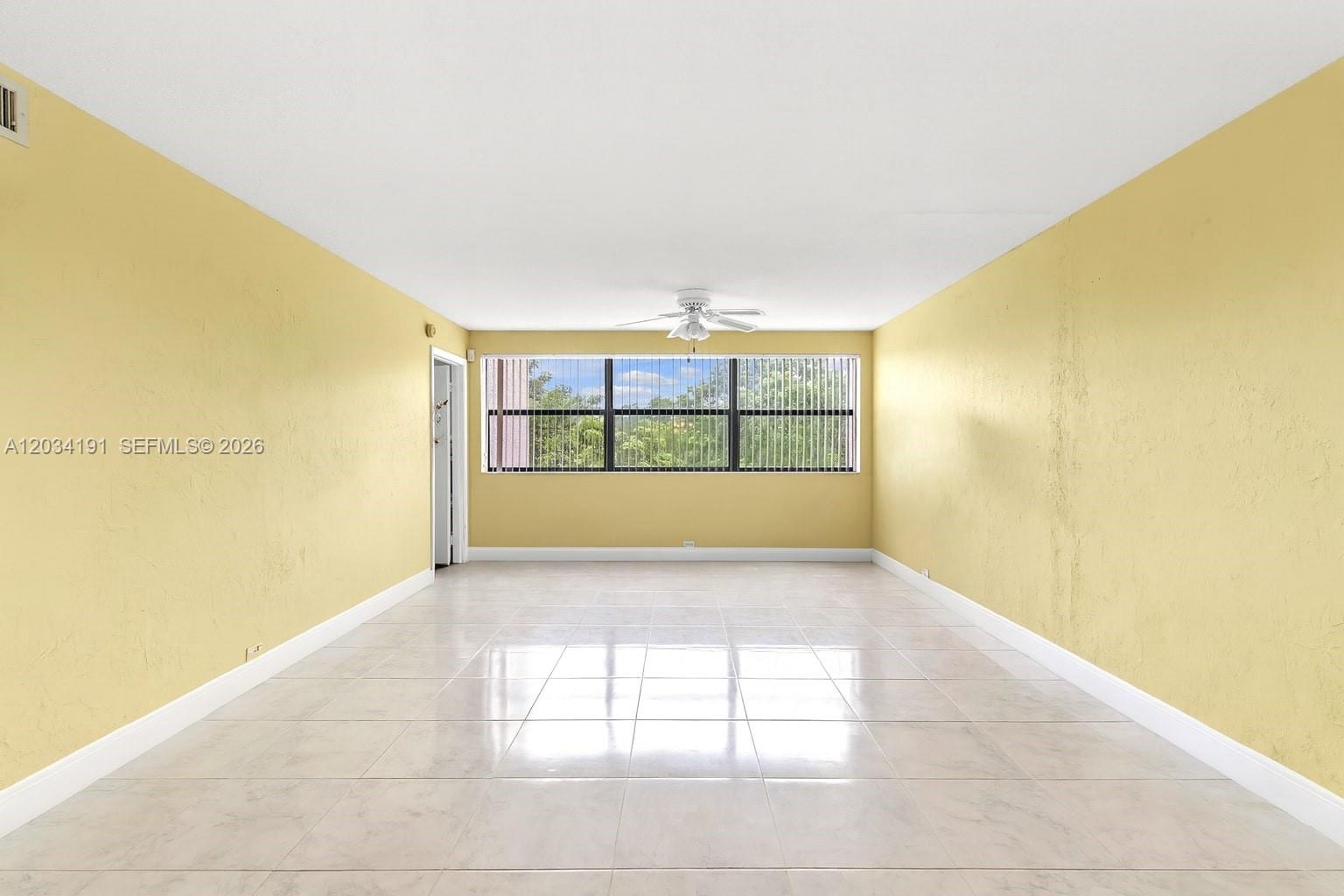 An empty room features yellow walls, white tile flooring, a ceiling fan, and a large window — 10400 NW 30th Ct # 305, Sunrise FL 33322, SUNRISE, FL