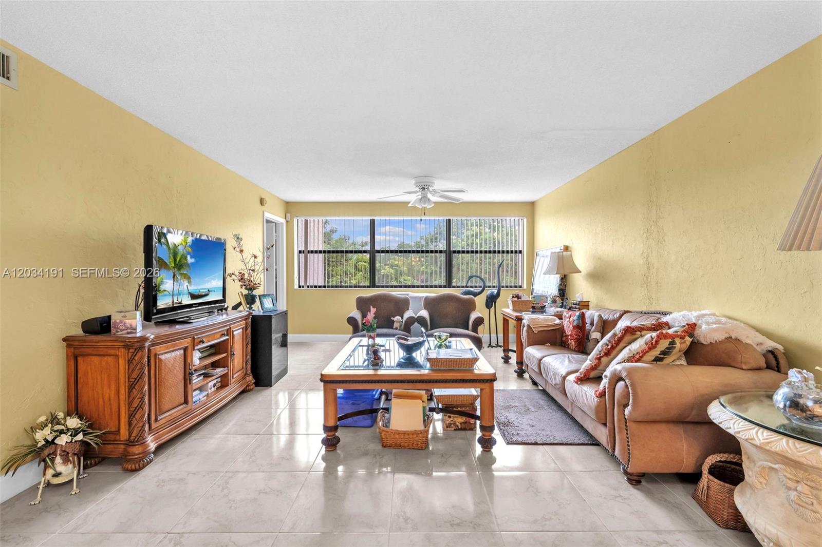 A living room features yellow walls, tile flooring, a brown sofa, and a television console — 10400 NW 30th Ct # 305, Sunrise FL 33322, SUNRISE, FL