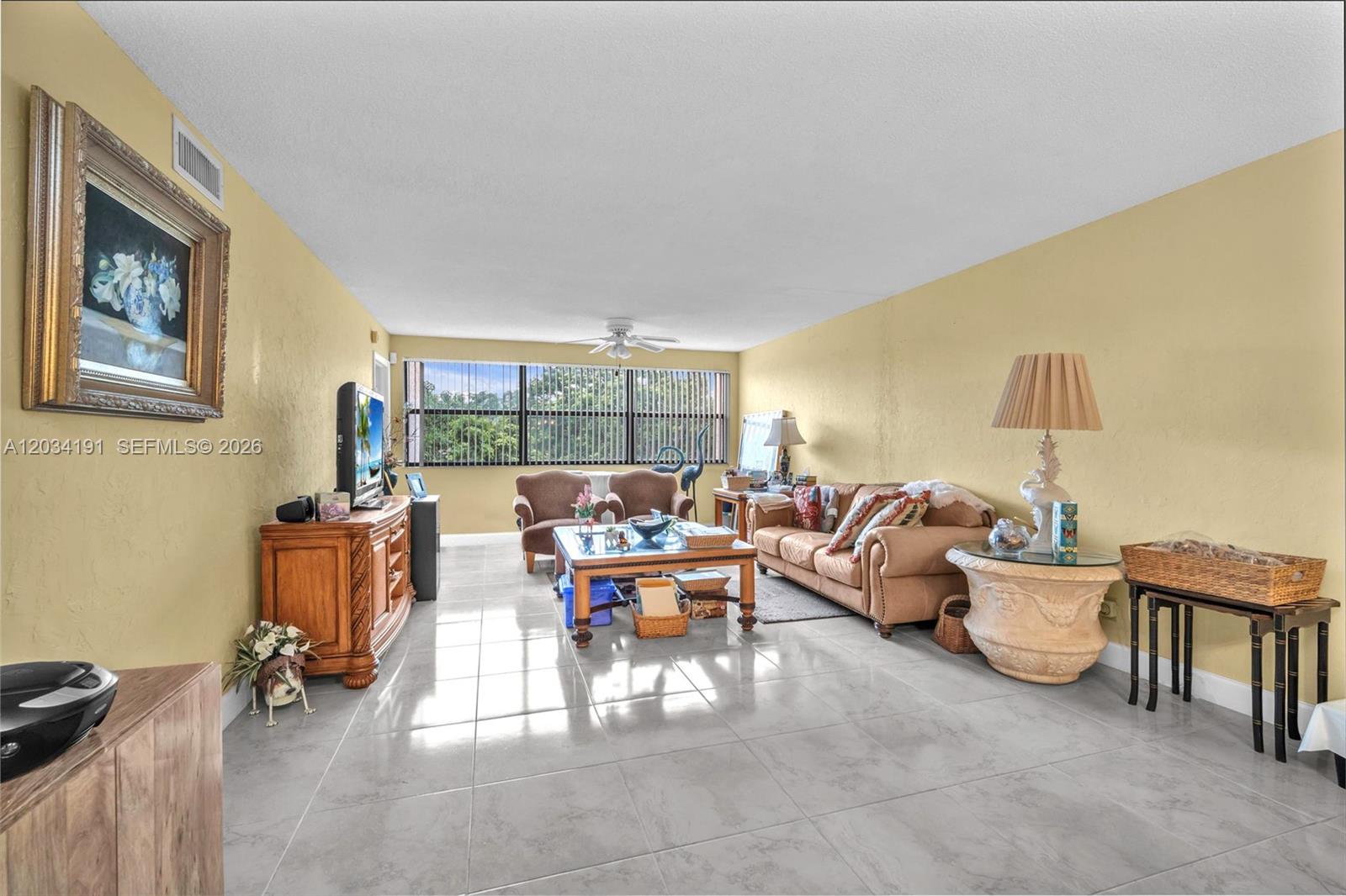 A living room features light yellow walls, tile flooring, a beige sofa, and large windows — 10400 NW 30th Ct # 305, Sunrise FL 33322, SUNRISE, FL