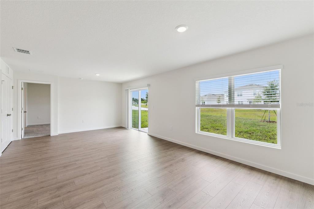 An empty living room features light wood-look flooring, white walls, recessed lighting, and sliding doors — 365 BASS COURT, POINCIANA, FL