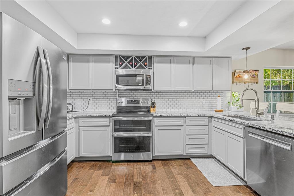 A kitchen with light gray cabinets, stainless steel appliances, white subway tile backsplash, and wood flooring — 612 NW 101ST STREET, GAINESVILLE, FL