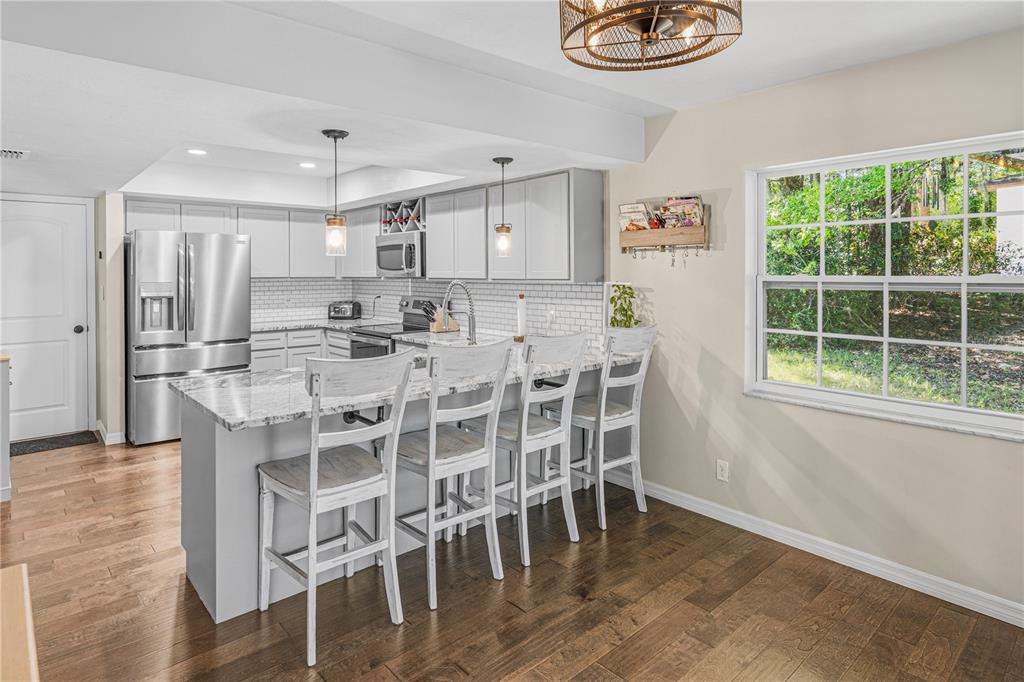 A kitchen with a granite-topped island, white cabinetry, stainless steel appliances, and wood flooring — 612 NW 101ST STREET, GAINESVILLE, FL