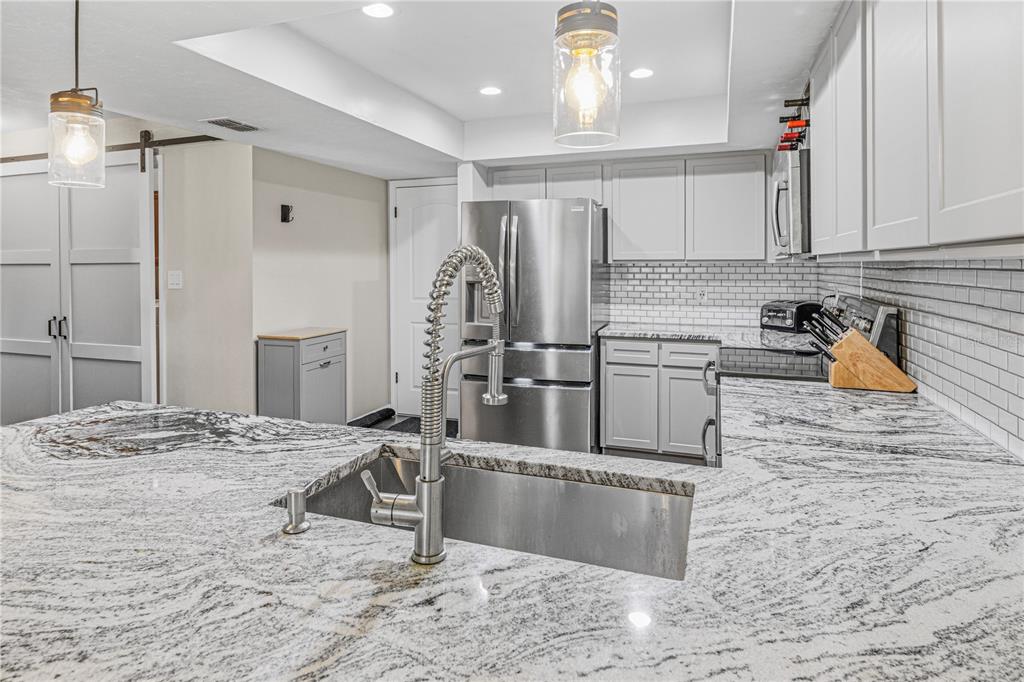 A kitchen features a granite-topped island with a sink, stainless steel appliances, and white cabinetry — 612 NW 101ST STREET, GAINESVILLE, FL