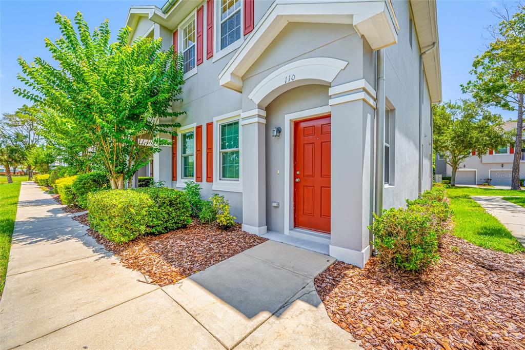 A two-story house exterior features a red front door, gray siding, and red shutters — 10409 CRIMSON PARK LANE UNIT 110, TAMPA, FL
