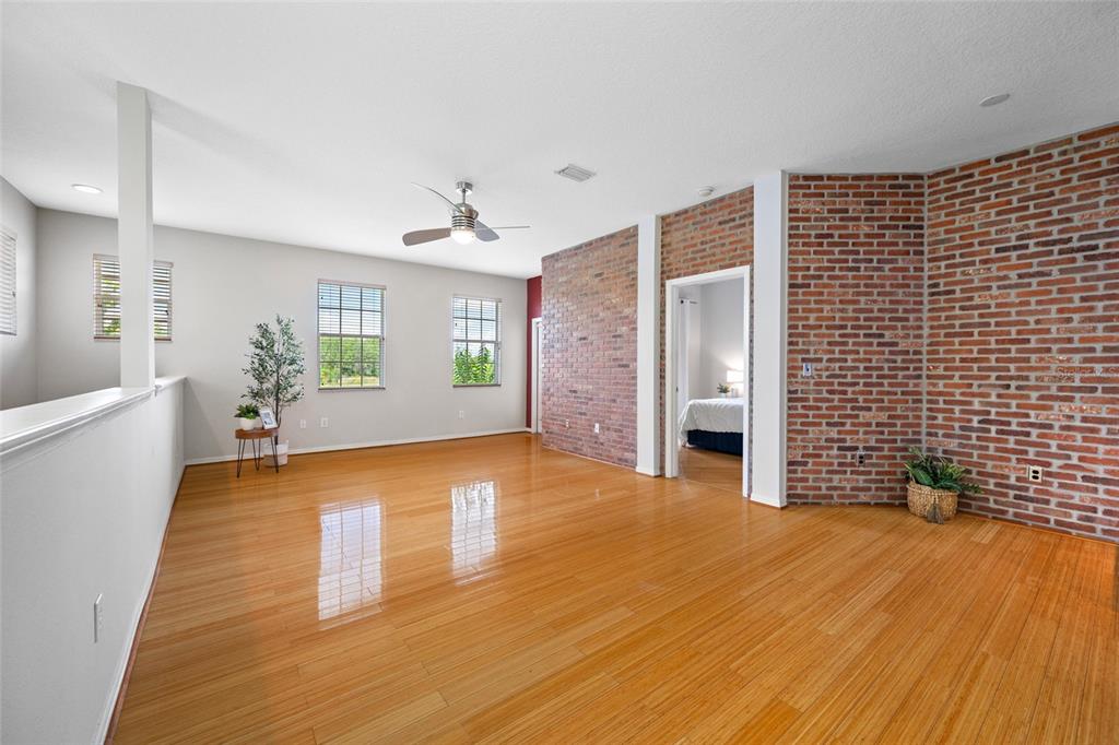A spacious room with light wood flooring, white walls, and a prominent exposed brick wall — 10409 CRIMSON PARK LANE UNIT 110, TAMPA, FL