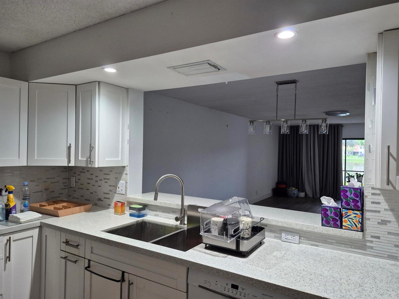 A kitchen with white cabinets, quartz countertops, and a pass-through window overlooking a living area — 9717 Sills Drive E # 102, Boynton Beach FL 33437, BOYNTON BEACH, FL
