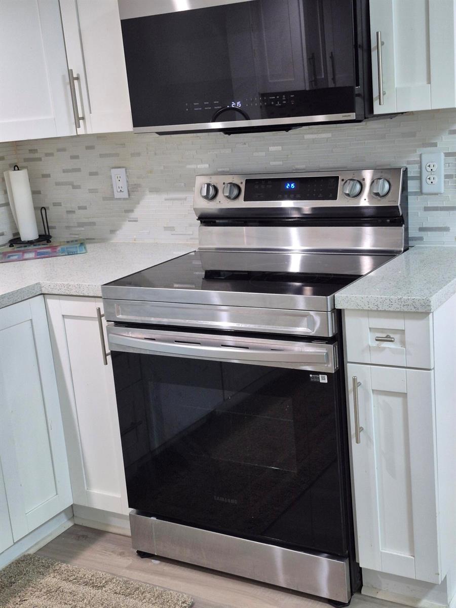 A kitchen features white cabinets, a stainless steel range, a microwave, and a tiled backsplash — 9717 Sills Drive E # 102, Boynton Beach FL 33437, BOYNTON BEACH, FL