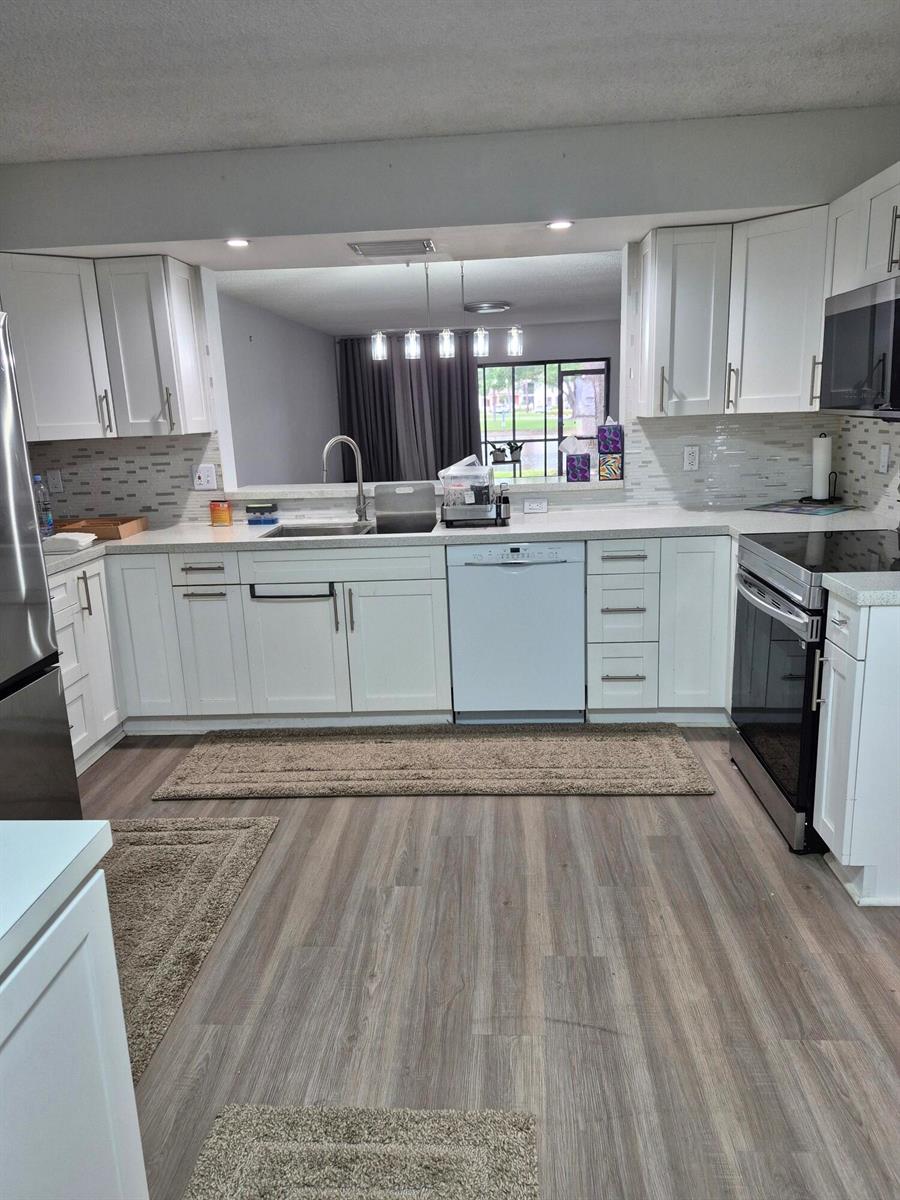 A kitchen with white cabinets, stainless steel appliances, and light wood-look flooring — 9717 Sills Drive E # 102, Boynton Beach FL 33437, BOYNTON BEACH, FL