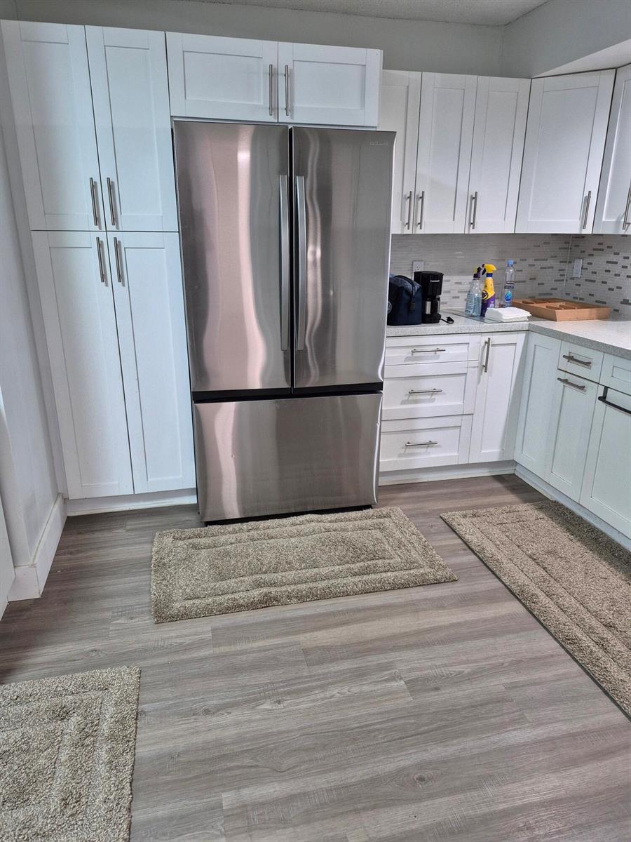 A kitchen features white cabinetry, stainless steel appliances, and gray wood-look flooring — 9717 Sills Drive E # 102, Boynton Beach FL 33437, BOYNTON BEACH, FL