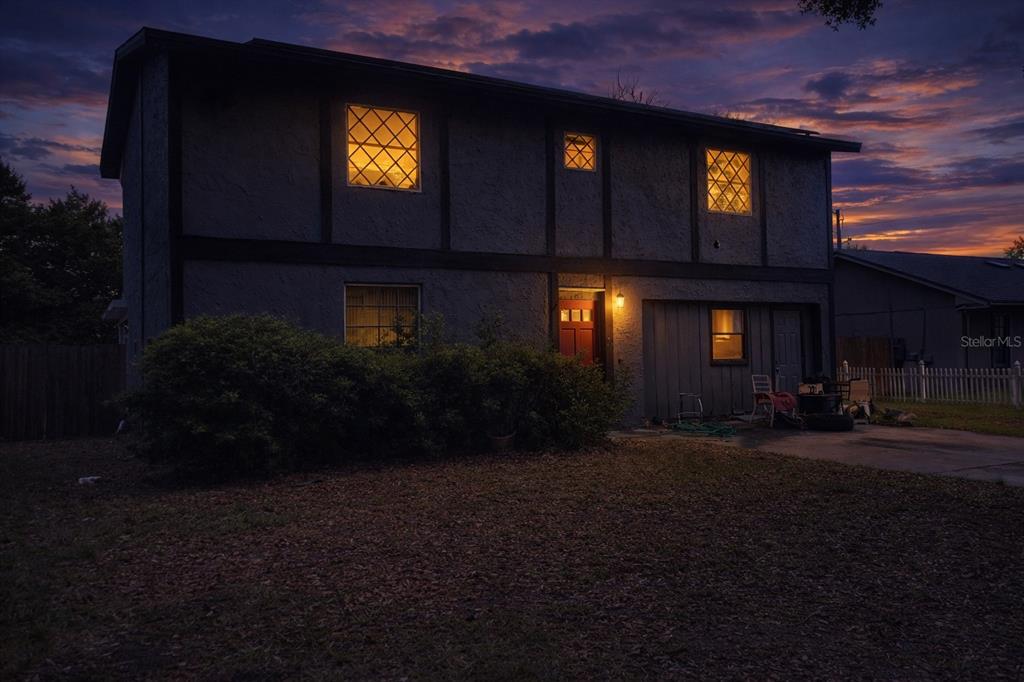A two-story house with dark stucco siding and a lit front entrance at dusk — 7393 GRAND AVENUE, WINTER PARK, FL